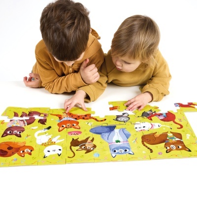 Duas crianças com camisolas castanhas a montar um puzzle colorido de cães e gatos.