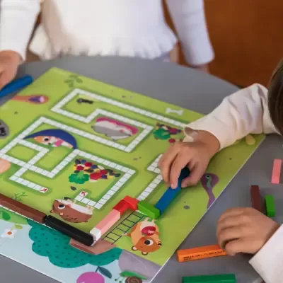 Jogo infantil de tabuleiro colorido com caminhos e peças retangulares coloridas sendo manuseadas por crianças