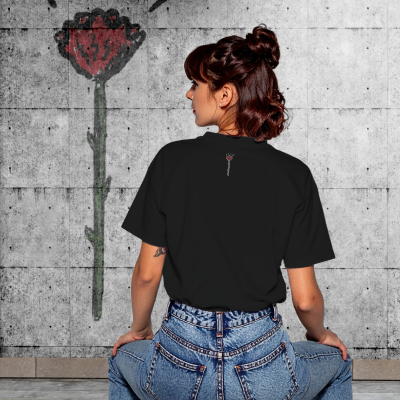 Mulher de costas com t-shirt preta e estampa de rosa vermelha, sentada em banco de madeira, parede de cimento com grafite de rosa ao fundo.