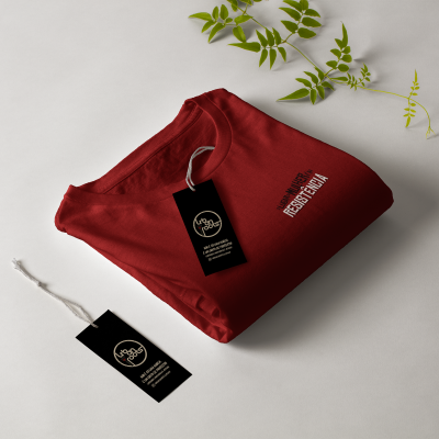 Camiseta vermelha dobrada com etiquetas pretas e folhas verdes ao fundo