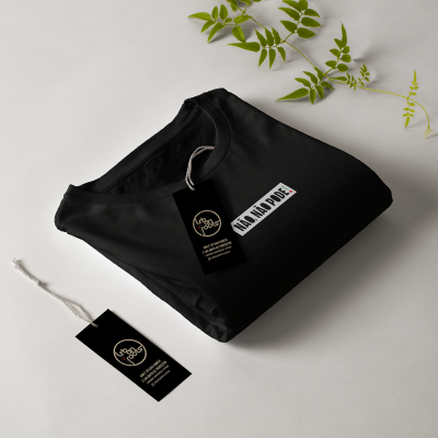 T-shirt preta dobrada com etiqueta preta e planta verde ao fundo