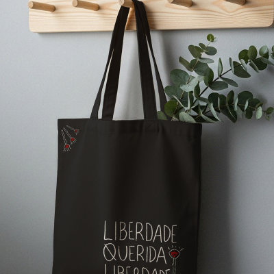 Saco de pano preto com texto e desenho de cravos pendurado em suporte de madeira