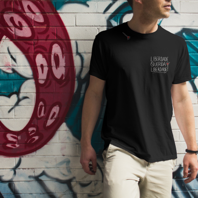 Homem com t-shirt preta com texto e flor, junto a parede grafitada colorida.