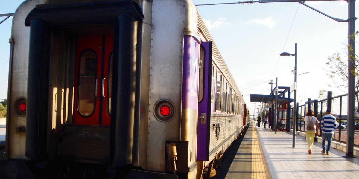 Comboio prateado com portas roxas numa plataforma de estação com passageiros a caminhar
