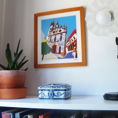 caixa de cerâmica azul e branca, planta em vaso, quadro colorido de igreja, luminária branca na parede