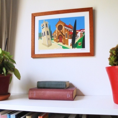 Quadro com ilustração de edifício histórico em parede branca, mesa branca com livros e plantas em vasos