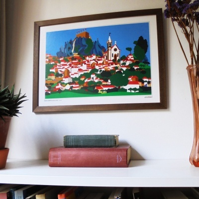 Ilustração colorida emoldurada de vila com igreja e castelo, livros empilhados, planta em vaso e vaso com flores secas