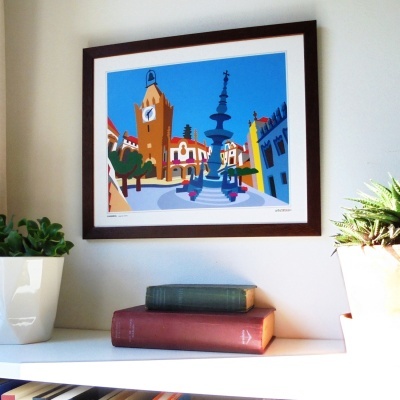 Pintura colorida em quadro de madeira sobre prateleira branca com livros e plantas