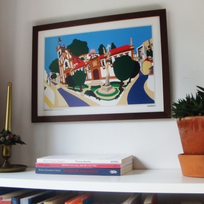 Quadro colorido pendurado numa parede acima de estante com livros e plantas em vasos terracota