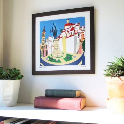 Moldura quadrada com gravura colorida de paisagem urbana, duas plantas em vasos e livros sobre prateleira branca