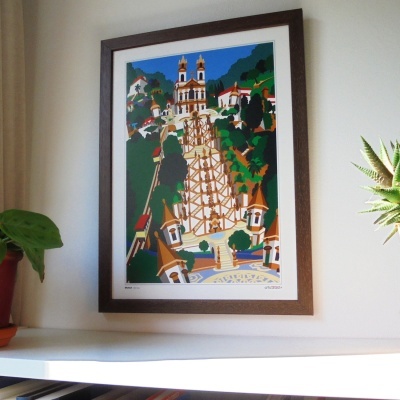 Quadro decorativo com arquitetura de igreja e escadaria em cores vivas, pendurado na parede branca junto a plantas