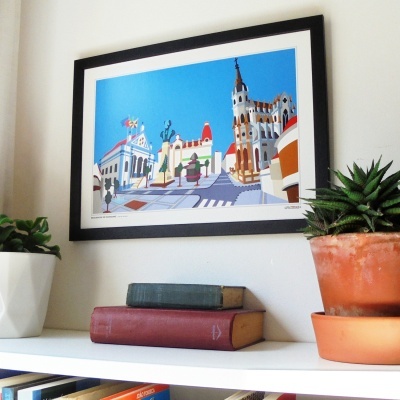 Quadro com ilustração urbana, livros empilhados e plantas suculentas numa prateleira branca