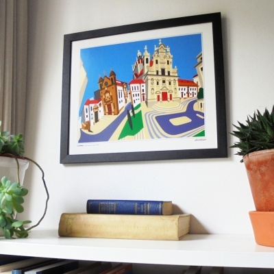 Gravura colorida emoldurada de edifícios históricos sobre estante com livros e plantas