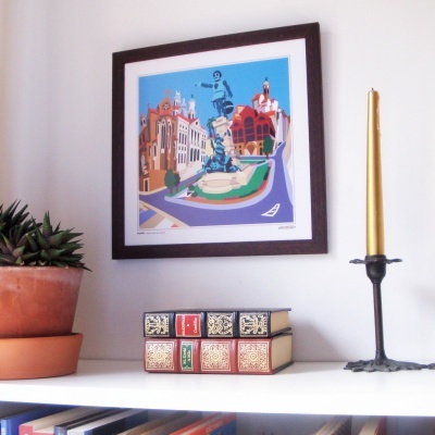 Prateleira com planta, livros, vela dourada e quadro colorido numa parede branca