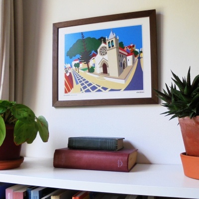 Quadro colorido de igreja e casas, plantas em vasos e livros numa prateleira