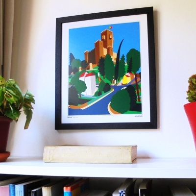 Poster ilustrado de castelo colorido em moldura preta numa parede, acima de prateleira com plantas e livros