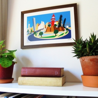 Quadro colorido de farol pendurado na parede com plantas e livros numa prateleira branca