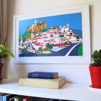 Quadro colorido de vila com castelo pendurado numa parede junto a plantas e livros numa estante