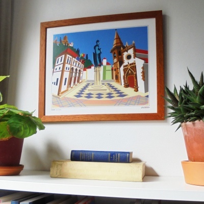Quadro ilustrativo colorido de praça pendurado em parede, com plantas em vasos e livros numa prateleira branca em primeiro plano