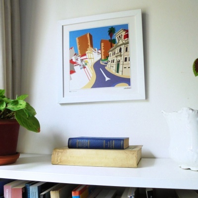 quadro ilustrativo de rua colorida pendurado sobre prateleira branca com livros e plantas