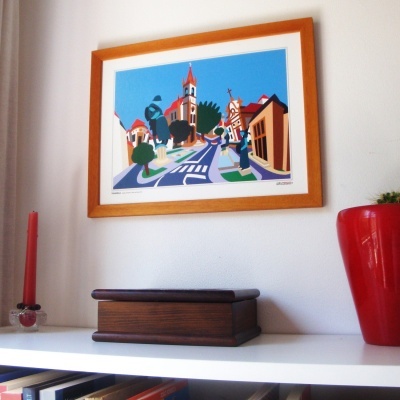 Ilustração colorida em quadro de madeira com casa e igreja, prateleira com caixa de madeira, castiçal e vaso vermelho