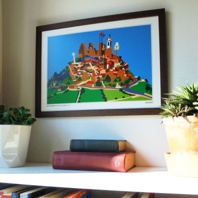 Quadro colorido de colina com edifícios numa parede com prateleira, livros e plantas