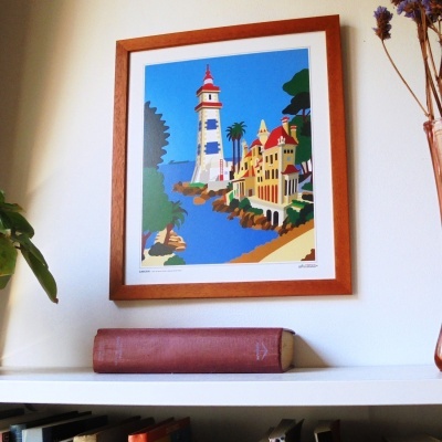 Quadro de farol com moldura de madeira acima de livro castanho numa prateleira branca