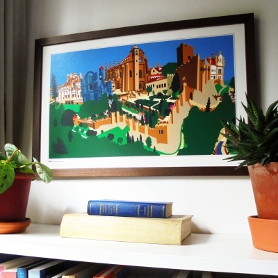Quadro colorido de castelo, plantas em vasos e livros numa prateleira branca