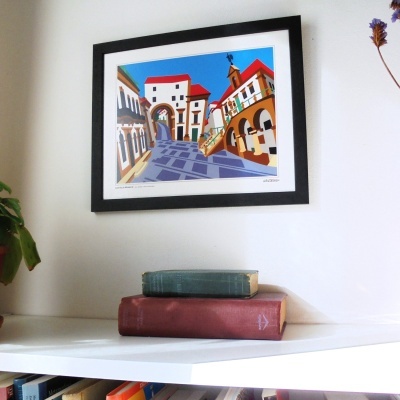 quadro colorido emoldurado pendurado na parede acima de prateleira com livros