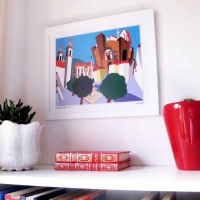 Quadro colorido emoldurado sobre prateleira com plantas em vasos branco e vermelho e livros vermelhos