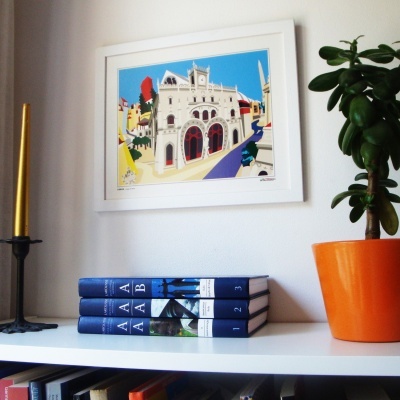 Estante branca com livros azuis, vela dourada, planta em vaso laranja e pintura colorida na parede