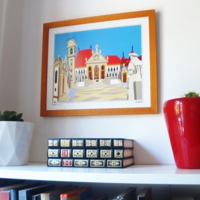 Quadro com pintura colorida de edifício histórico em moldura de madeira, vasos branco e vermelho e livros numa prateleira branca