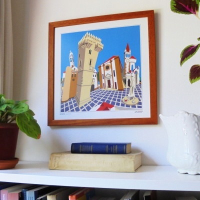 Quadro colorido de arquitetura com moldura de madeira em parede branca sobre estante com livros e jarra branca