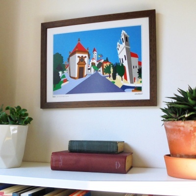 Quadro colorido pendurado numa parede branca com pintura de paisagem urbana e estante com livros e plantas