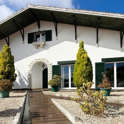 Moradia branca com janelas verdes e jardim com plantas em vasos