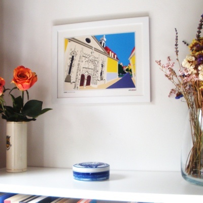 quadro de igreja colorida na parede branca com vasos e prateleira