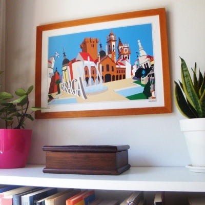 Quadro colorido com ilustração de Braga numa parede branca com plantas e caixa de madeira numa prateleira