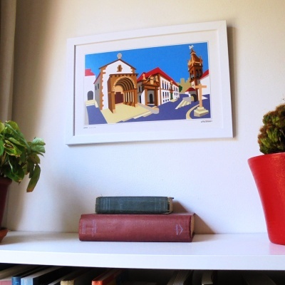 Quadro colorido de edifícios históricos pendurado numa parede acima de livros e plantas em prateleira