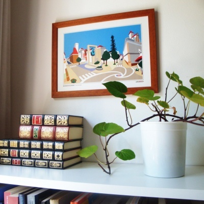Quadro colorido, planta em vaso branco, livros decorativos numa estante branca