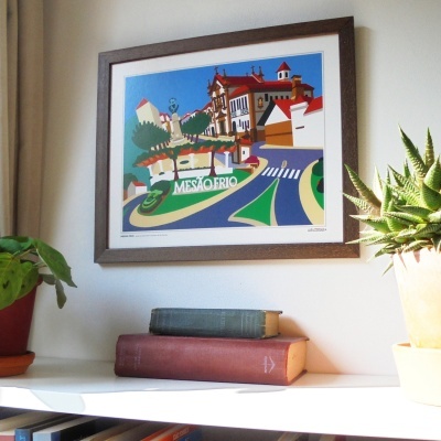 Quadro decorativo de Mesão Frio, moldura escura, em parede clara acima de prateleira com livros e plantas