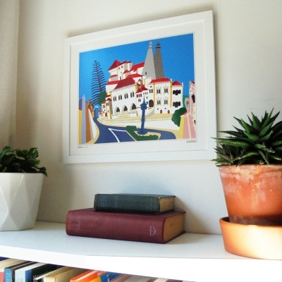quadro decorativo de edifícios coloridos na parede com prateleira branca, livros e vasos de plantas