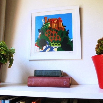 Quadro colorido de castelo em parede branca com livros antigos e plantas em estante branca