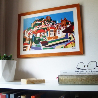 Quadro colorido com moldura de madeira na parede sobre estante branca com livros e planta