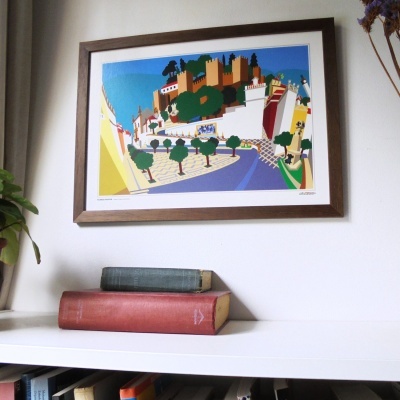 Quadro colorido abstrato de cidade e livros antigos empilhados numa prateleira branca.