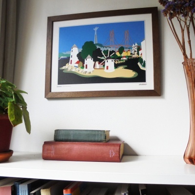 Quadro decorativo com moinhos de vento e ponte vermelha na parede acima de prateleira com livros