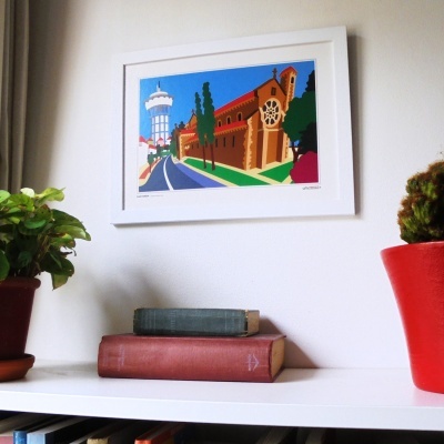 quadro colorido de rua com torre e edifícios, dois livros antigos e plantas em vasos em prateleira branca