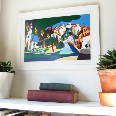 Quadro colorido em moldura branca com ilustração abstrata de cidade acima de prateleira com plantas e livros.