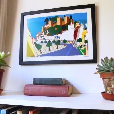 Quadro com ilustração colorida de uma paisagem com castelo e árvores em moldura preta