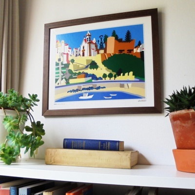 Quadro com paisagem urbana estilizada, moldura castanha, estante branca com livros e plantas