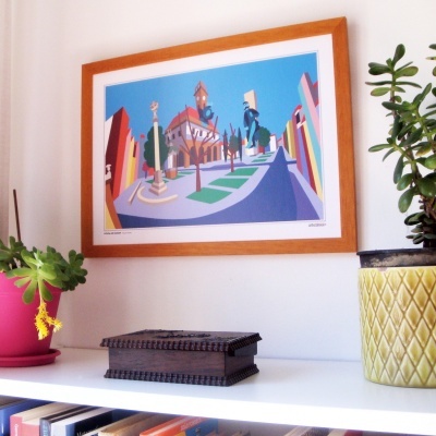 Quadro colorido de praça urbana com moldura de madeira na parede acima de prateleira com plantas e caixa de madeira